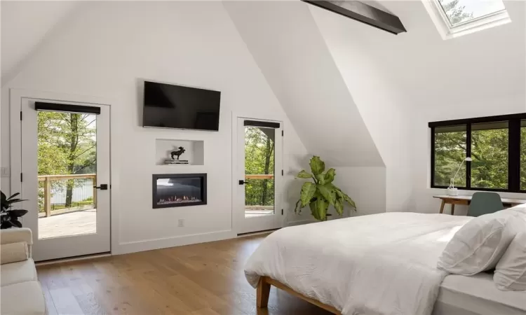 Bedroom with light hardwood / wood-style floors, access to exterior, high vaulted ceiling, and a skylight