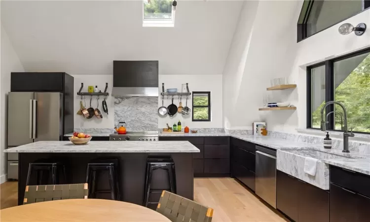 Kitchen featuring appliances with stainless steel finishes, wall chimney exhaust hood, light stone counters, and plenty of natural light