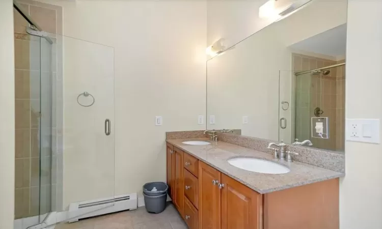 Bathroom featuring vanity, tile patterned flooring, baseboard heating, and a shower with door