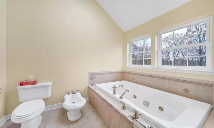 Bathroom with toilet, tile patterned flooring, a bidet, tiled tub, and vaulted ceiling