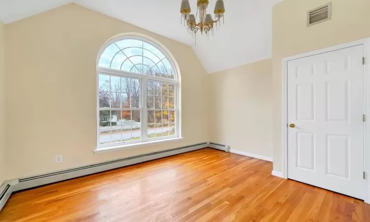 Empty room featuring light hardwood / wood-style flooring, a baseboard heating unit, a chandelier, and vaulted ceiling