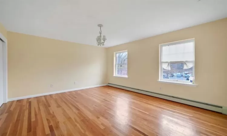 Spare room with light hardwood / wood-style flooring, a baseboard heating unit, and a notable chandelier