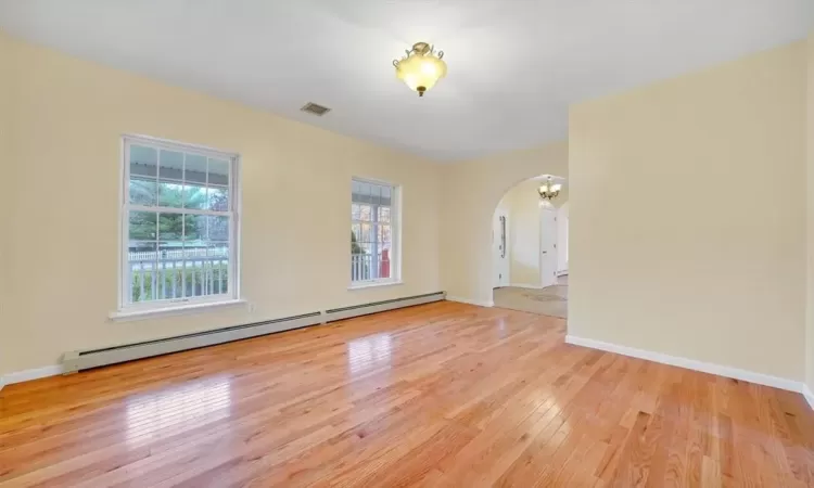 Unfurnished room featuring a baseboard heating unit, a chandelier, light wood-type flooring, and a wealth of natural light