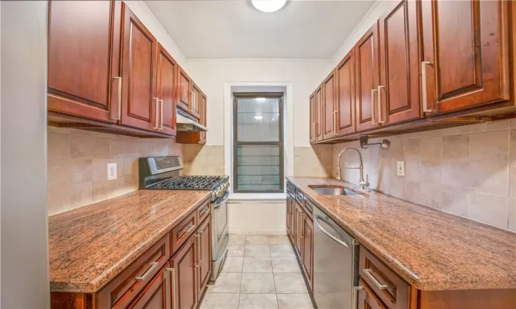 Kitchen with dark stone counters, sink, light tile patterned floors, backsplash, and appliances with stainless steel finishes