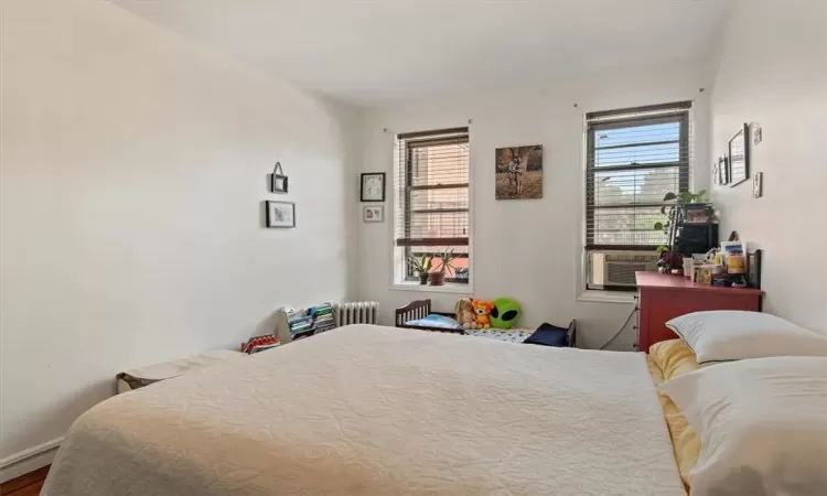 Bedroom with radiator heating unit, multiple windows, hardwood / wood-style flooring, and cooling unit