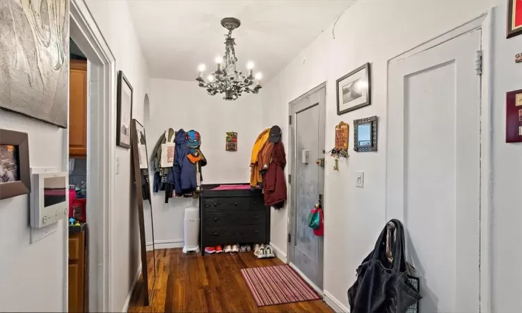 Corridor featuring dark wood-type flooring and a notable chandelier