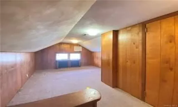 Bonus room with wood walls, light carpet, and lofted ceiling