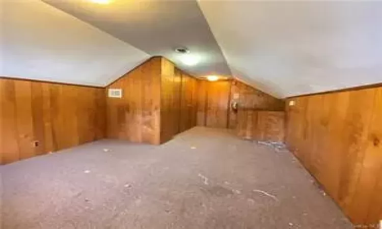 Bonus room with wood walls, lofted ceiling, and carpet