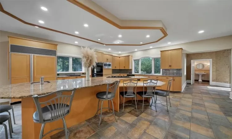 Kitchen with light brown cabinets, a kitchen breakfast bar, built in appliances, and a center island