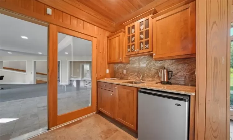 Lower level kitchen featuring sink, light stone counters, stainless steel dishwasher, tasteful backsplash, and light tile patterned floors