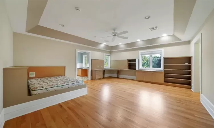 HANDICAPPED ACCESSIBLE Bedroom/shelving and bathroom, with light hardwood / wood-style floors, a raised ceiling, ceiling fan.