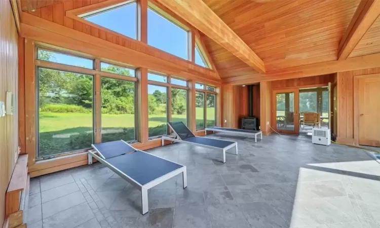 Sunroom / solarium with plenty of natural light, beamed ceiling, and a wood stove