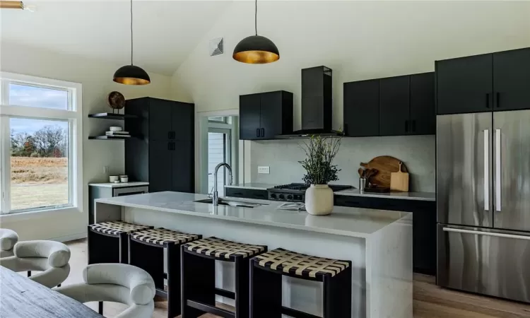 Kitchen featuring stainless steel refrigerator, exhaust hood, hanging light fixtures, sink, and light hardwood / wood-style floors