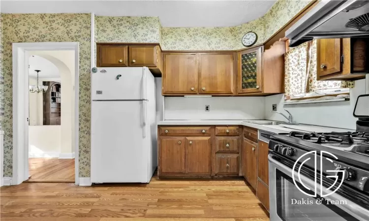 Kitchen featuring stainless steel gas range, white fridge, light hardwood / wood-style floors, and exhaust hood