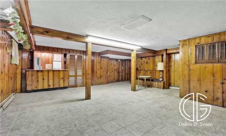 Basement with wood walls, a textured ceiling, and a baseboard heating unit