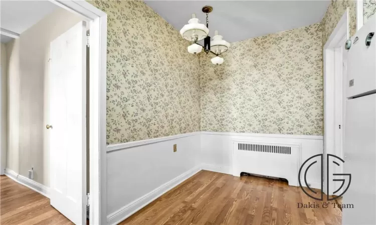 Unfurnished dining area with hardwood / wood-style floors, radiator, and a notable chandelier