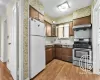 Kitchen featuring white fridge, range hood, light wood-type flooring, dishwashing machine, and stainless steel range with gas stovetop