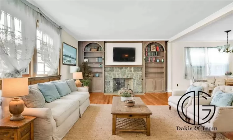 Living room featuring built in features, crown molding, a fireplace, light wood-type flooring, and an inviting chandelier