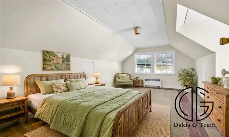 Bedroom with radiator heating unit, lofted ceiling, and light hardwood / wood-style flooring