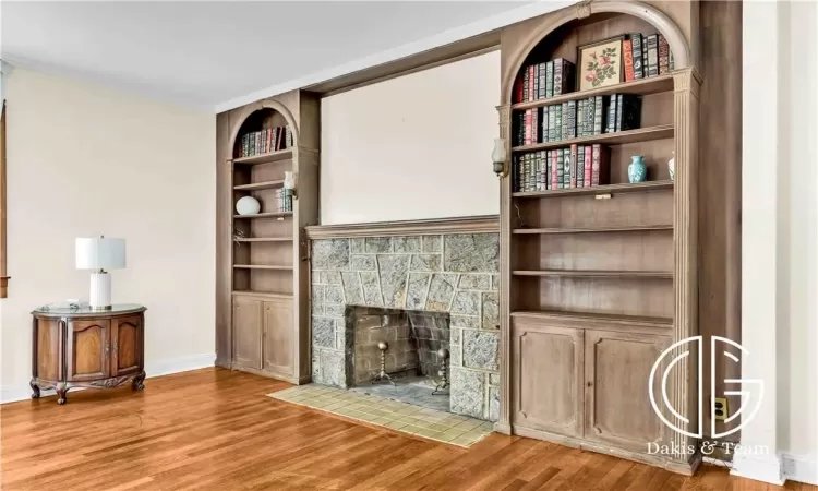 Living room with a stone fireplace, built in features, hardwood / wood-style floors, and crown molding