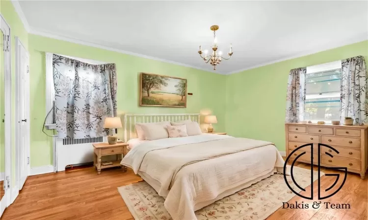 Bedroom with radiator heating unit, light hardwood / wood-style flooring, crown molding, and a notable chandelier