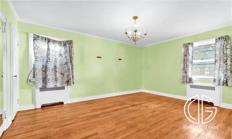 Unfurnished room with radiator, a chandelier, wood-type flooring, and ornamental molding