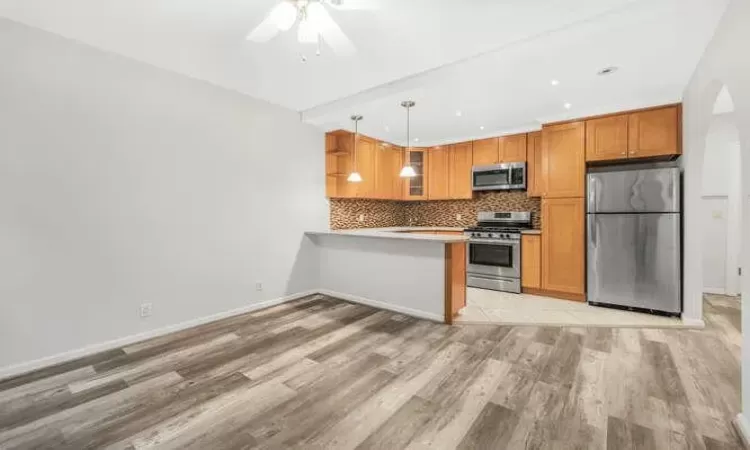 Kitchen with kitchen peninsula, appliances with stainless steel finishes, backsplash, pendant lighting, and light hardwood / wood-style flooring