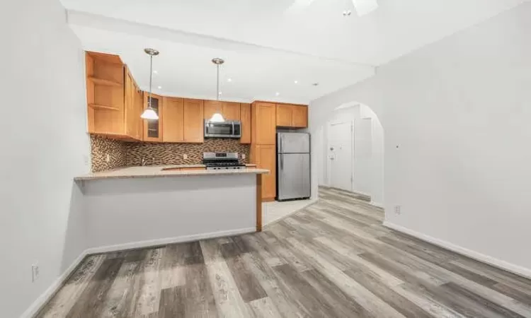 Kitchen with hanging light fixtures, light hardwood / wood-style flooring, tasteful backsplash, kitchen peninsula, and stainless steel appliances