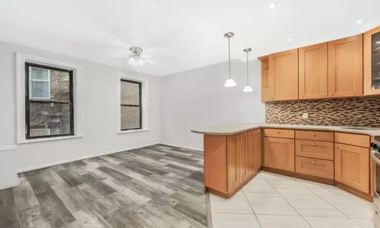 Kitchen featuring kitchen peninsula, decorative backsplash, light wood-type flooring, ceiling fan, and pendant lighting