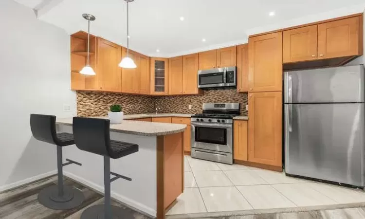 Kitchen featuring backsplash, decorative light fixtures, a breakfast bar, appliances with stainless steel finishes, and ornamental molding