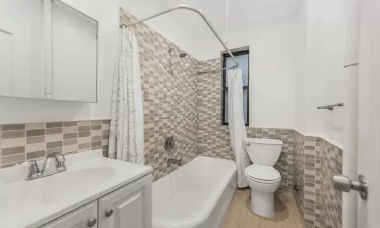 Full bathroom with vanity, shower / bathtub combination with curtain, toilet, and tile walls