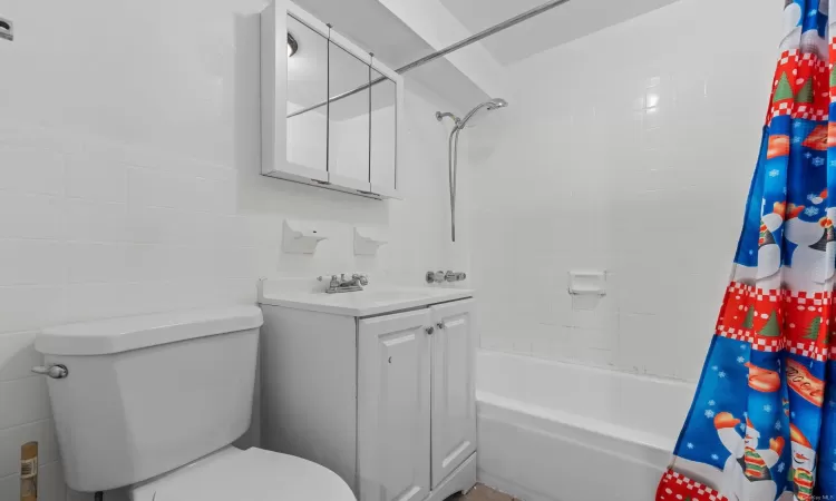 Full bathroom featuring toilet, tile walls, vanity, and shower / tub combo with curtain