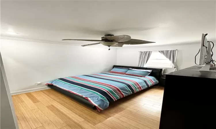 Bedroom with ceiling fan, ornamental molding, and wood-type flooring