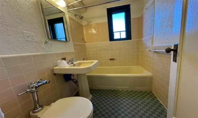 Full bathroom featuring sink, a textured ceiling, toilet, tile walls, and tiled shower / bath combo