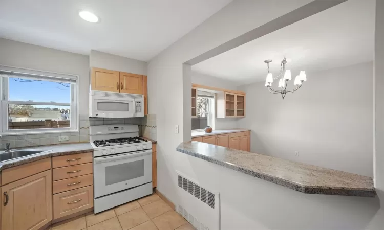 Kitchen featuring sink, light brown cabinets, white appliances, pendant lighting, and a notable chandelier