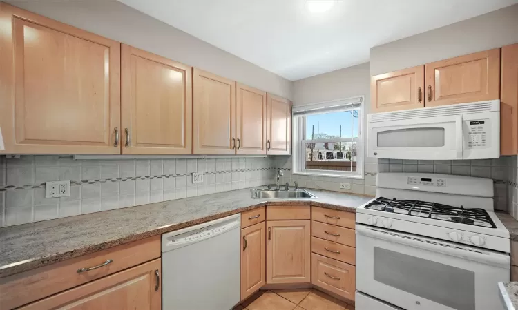 Kitchen featuring sink, white appliances, light tile patterned floors, decorative backsplash, and light brown cabinetry