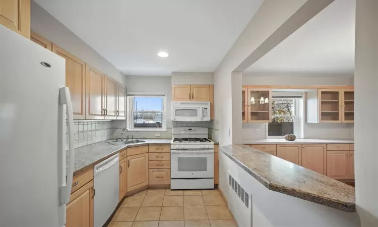 Kitchen featuring sink, light brown cabinets, white appliances, light tile patterned floors, and decorative backsplash