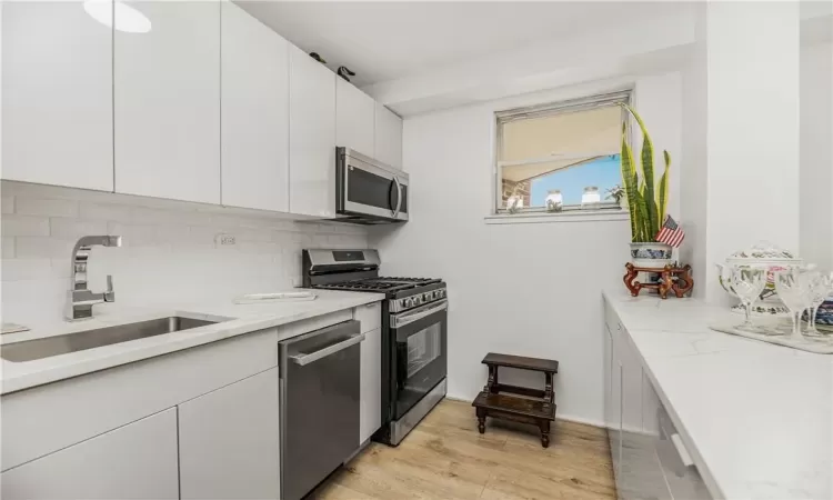 Kitchen featuring appliances with stainless steel finishes, white cabinets, light hardwood / wood-style floors, tasteful backsplash, and sink