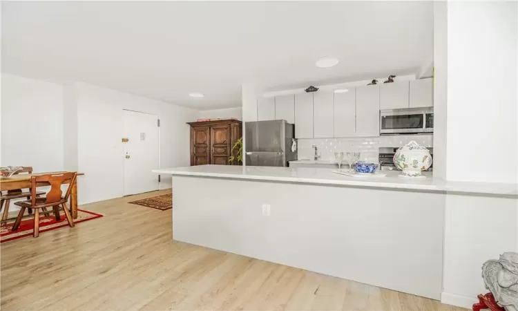 Kitchen with appliances with stainless steel finishes, white cabinets, light hardwood / wood-style flooring, decorative backsplash, and kitchen peninsula