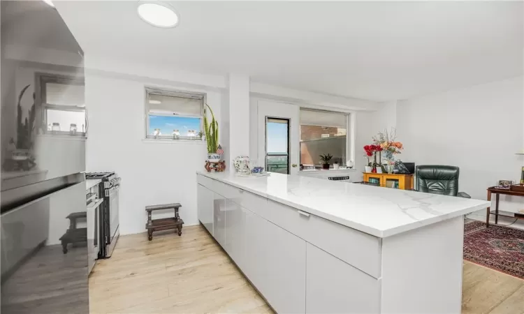 Kitchen featuring light wood-type flooring, stainless steel range with gas cooktop, kitchen peninsula, and light stone countertops