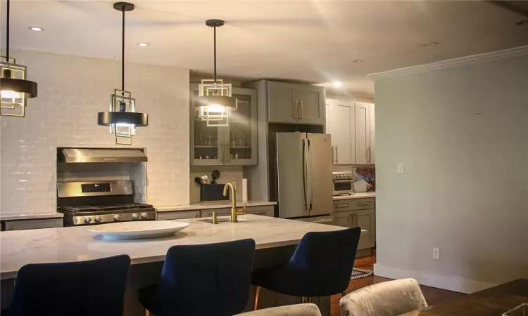 Kitchen featuring appliances with stainless steel finishes, wall chimney range hood, hanging light fixtures, backsplash, and a breakfast bar area