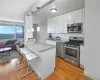 Kitchen with a breakfast bar, light hardwood / wood-style flooring, white cabinets, light stone counters, and appliances with stainless steel finishes