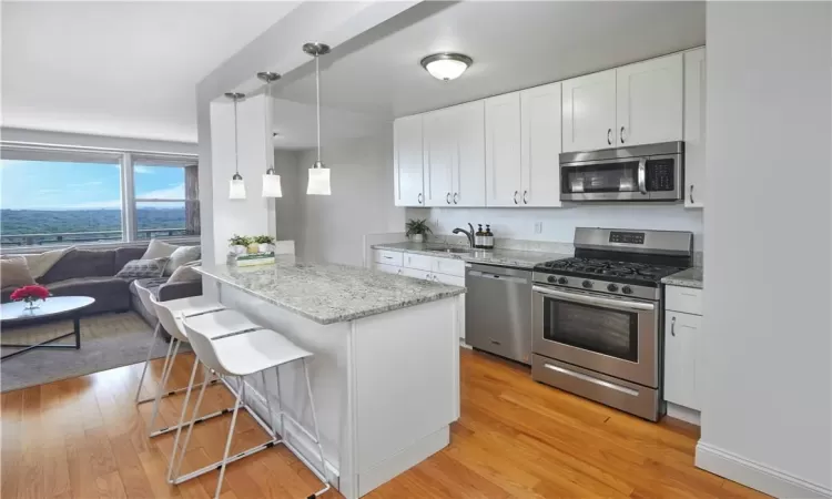 Kitchen with a breakfast bar, light hardwood / wood-style flooring, white cabinets, light stone counters, and appliances with stainless steel finishes