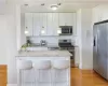 Kitchen with appliances with stainless steel finishes, light hardwood / wood-style flooring, a breakfast bar, light stone countertops, and white cabinetry