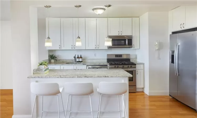 Kitchen with appliances with stainless steel finishes, light hardwood / wood-style flooring, a breakfast bar, light stone countertops, and white cabinetry