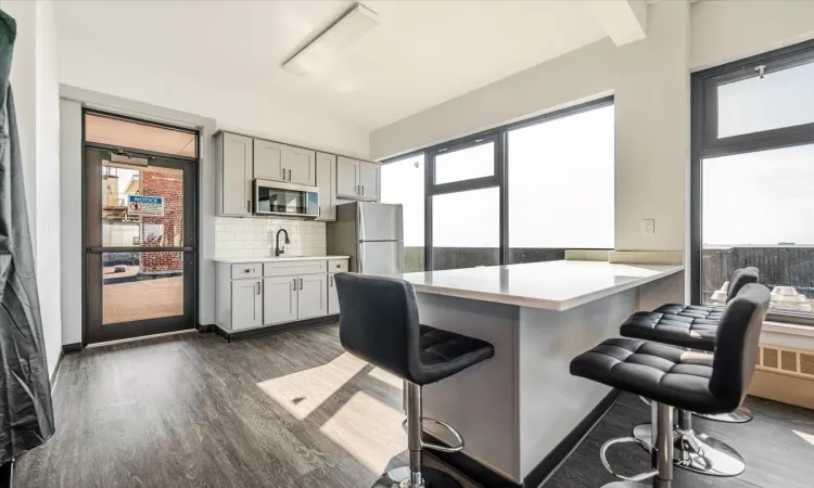 Kitchen with backsplash, dark wood-type flooring, a kitchen breakfast bar, kitchen peninsula, and stainless steel appliances