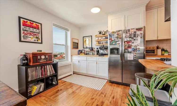 Kitchen with decorative backsplash, stainless steel refrigerator with ice dispenser, white cabinets, radiator heating unit, and light hardwood / wood-style floors