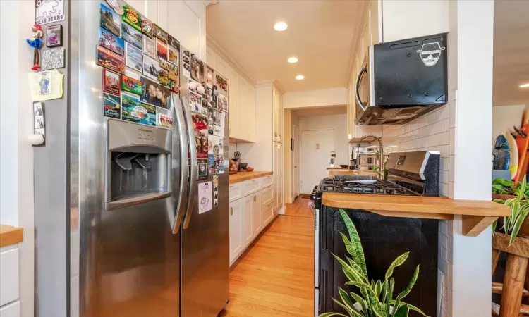 Kitchen featuring stainless steel appliances, butcher block counters, light hardwood / wood-style floors, white cabinetry, and a breakfast bar area