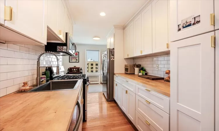 Kitchen featuring white cabinets, wood counters, light hardwood / wood-style floors, and stainless steel appliances