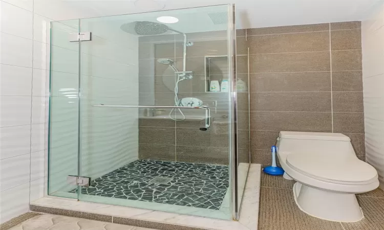 Bathroom featuring toilet, tile walls, and a shower with shower door